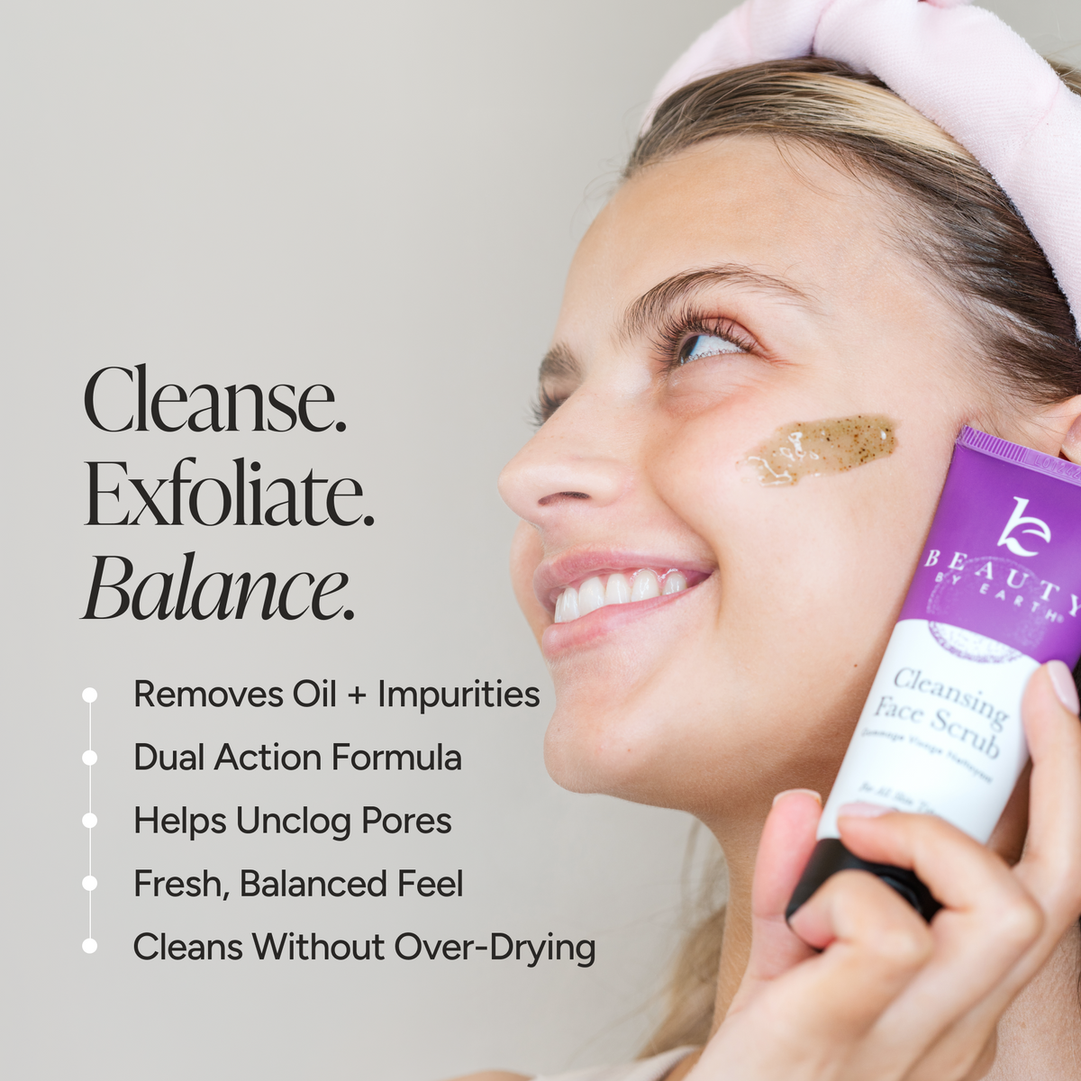 A woman in profile applies a brown scrub to her cheek while holding a purple and white Beauty by Earth Cleansing Face Scrub.