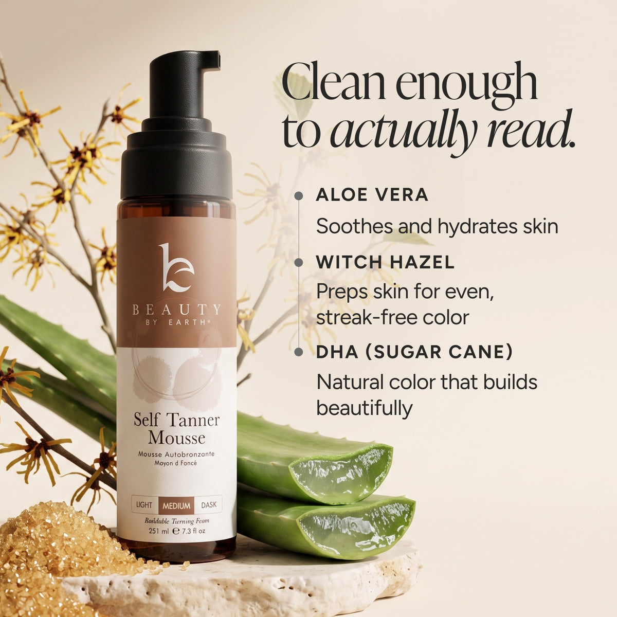 A bottle of Beauty by Earths Self Tanner Mousse is displayed on a stone slab with aloe vera leaves and sand. The background is a warm beige with text detailing the ingredients (Aloe Vera, Witch Hazel, DHA (Sugarcane)) and a tagline 'Clean enough to actually read.