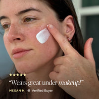 Close-up of a woman applying sunscreen serum to her cheek, with text overlay reading 'Wears great under makeup!' and 'MEGAN H. Verified Buyer'.