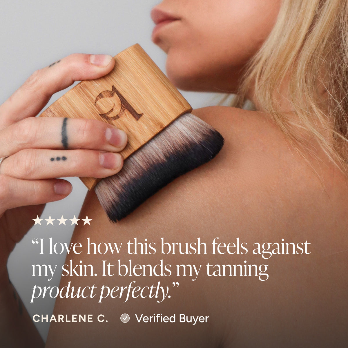A close-up of a woman applying a tanning product with a rectangular wooden brush. A customer review quote by Charlene C.