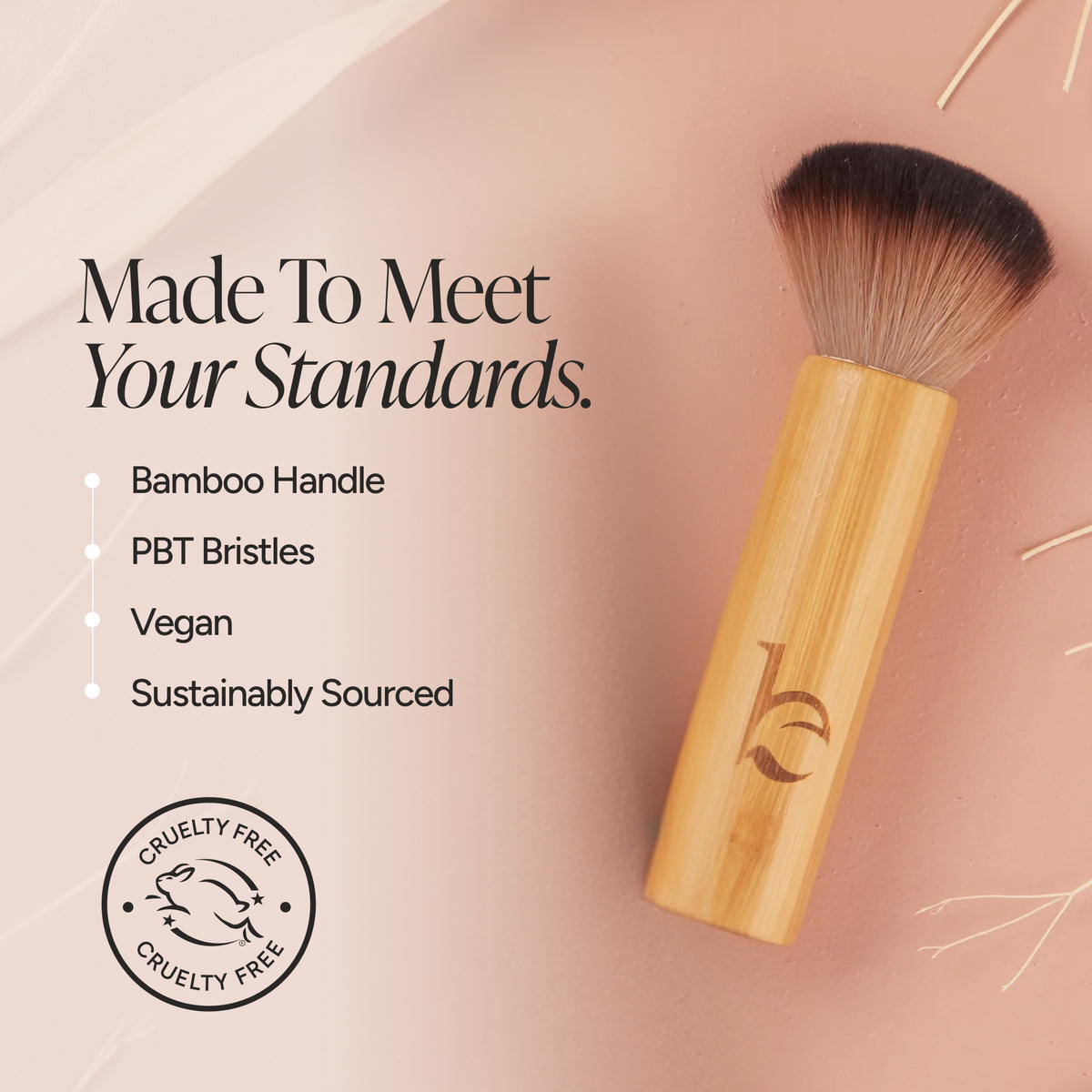 A brush with a light bamboo handle and dark bristles, shown on a soft peach background with marketing text and a cruelty-free seal. The text highlights a bamboo handle, PBT bristles, vegan formula, and sustainably sourced materials.
