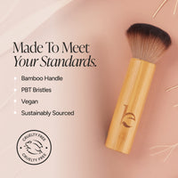 A brush with a light bamboo handle and dark bristles, shown on a soft peach background with marketing text and a cruelty-free seal. The text highlights a bamboo handle, PBT bristles, vegan formula, and sustainably sourced materials.