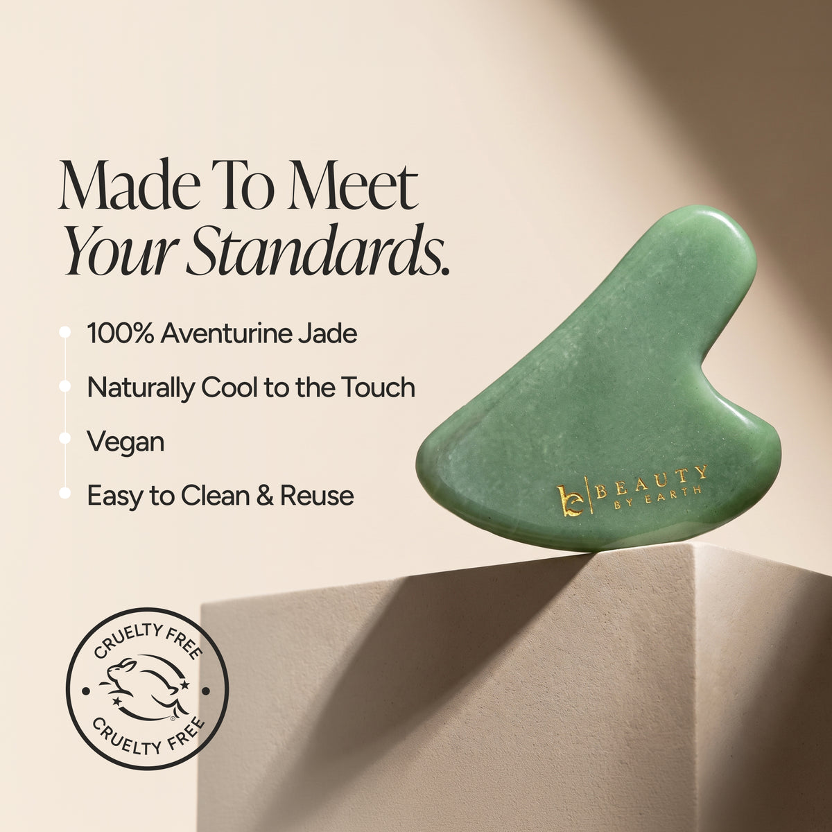 A green gua sha massage tool made of aventurine jade, displayed on a beige pedestal with promotional text and a cruelty-free seal. The brand name 'Beauty by Earth' is printed in gold on the tool.