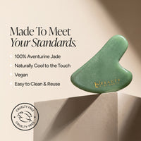 A green gua sha massage tool made of aventurine jade, displayed on a beige pedestal with promotional text and a cruelty-free seal. The brand name 'Beauty by Earth' is printed in gold on the tool.