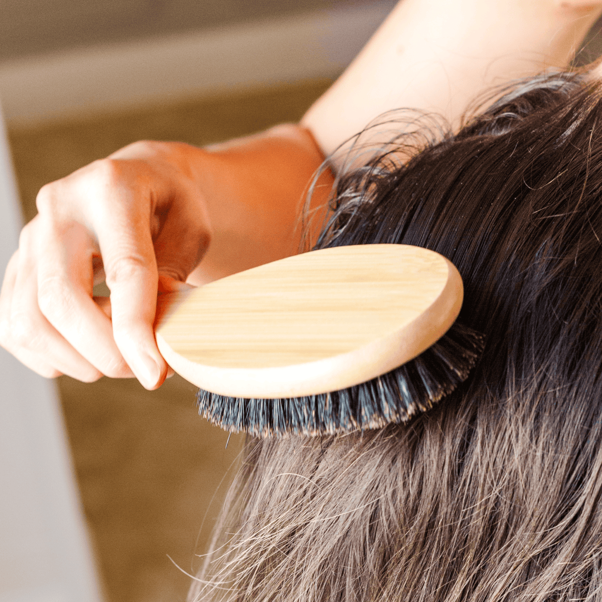 Person using a wooden hairbrush on their hair
