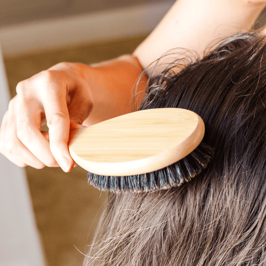 Person using a wooden hairbrush on their hair