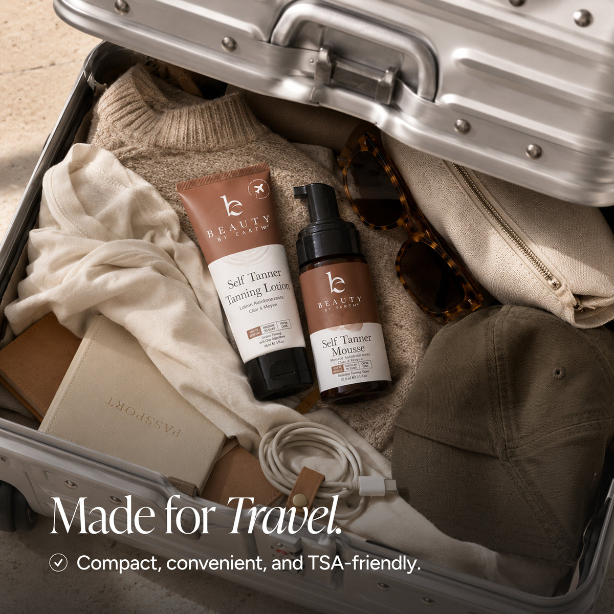 Beauty by Earth selt tanning products arranged inside an open silver suitcase with travel items, including a sweater, sunglasses, a cap, a pouch, and a phone cable. Text at the bottom reads, 'Made for Travel.