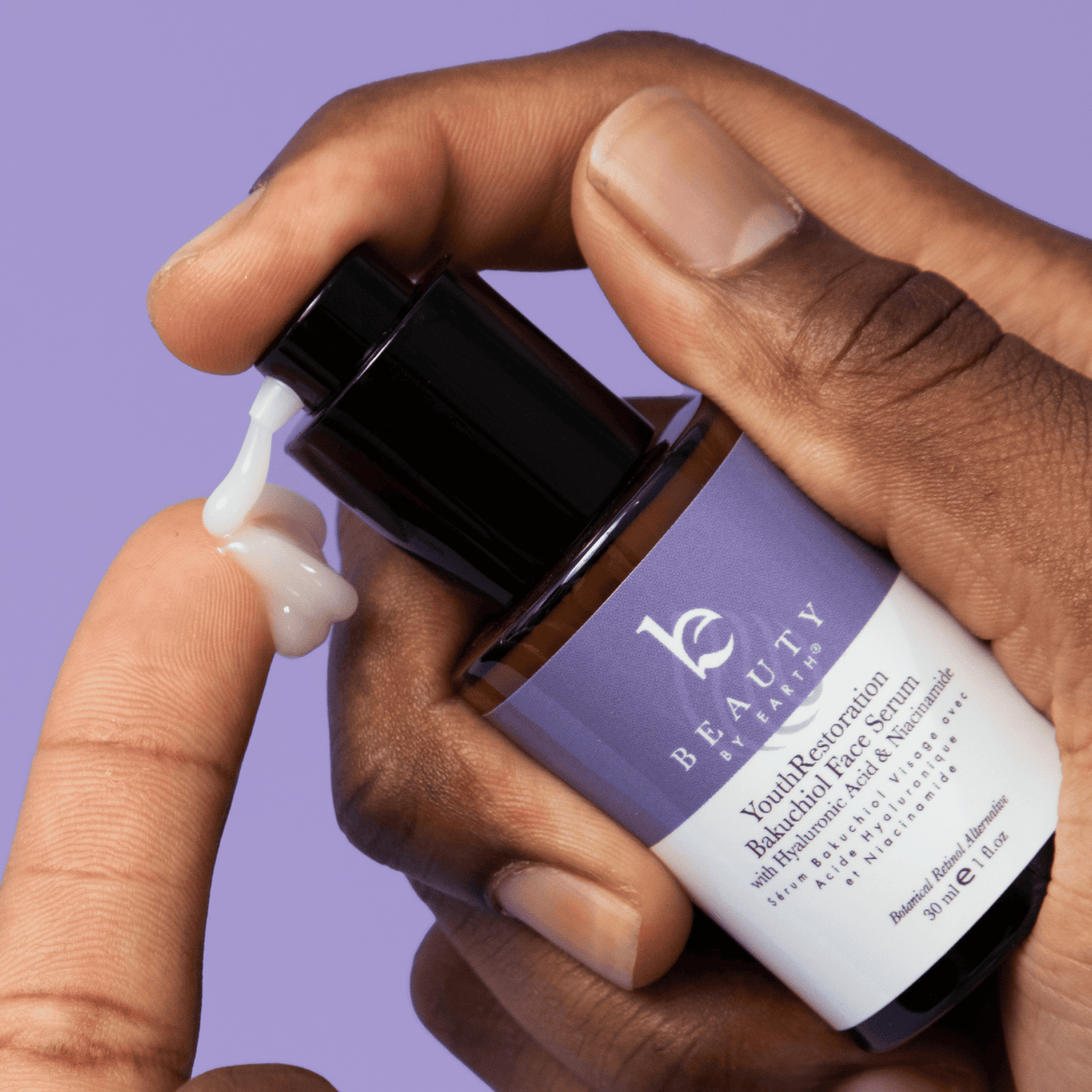 Hand applying a skincare serum from a bottle labeled 'Beauty That Is' against a purple background