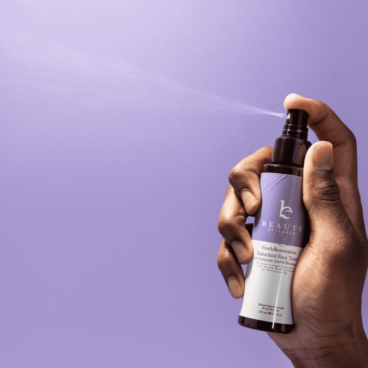 Hand holding a bottle of 'beauty by...' face toner against a purple background