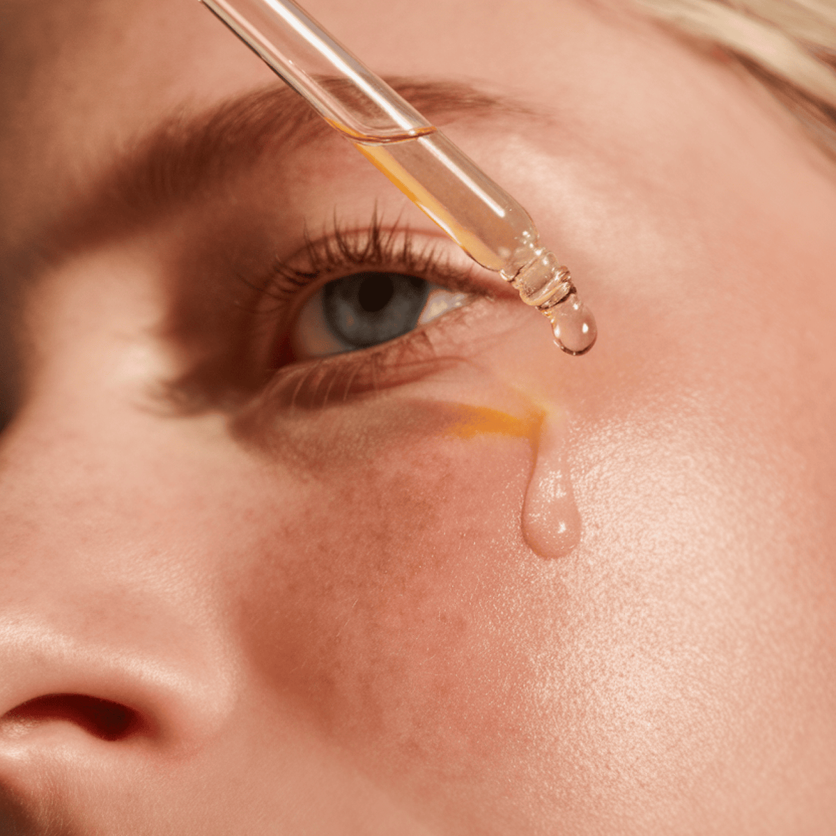 Close-up of a dropper with a drop of liquid being applied to a person's skin.