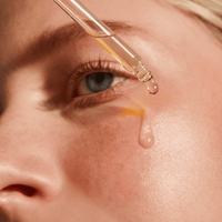 Close-up of a dropper with a drop of liquid being applied to a person's skin.