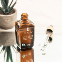 Bottle of Balance & Restore Luxury Face Oil with dropper on a reflective surface.