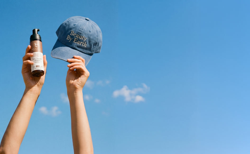Person holding a blue cap and self tanner bottle against a clear blue sky