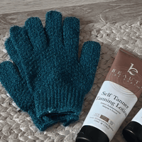 Medium exfoliating gloves and a tube of self tanning lotion on a textured surface
