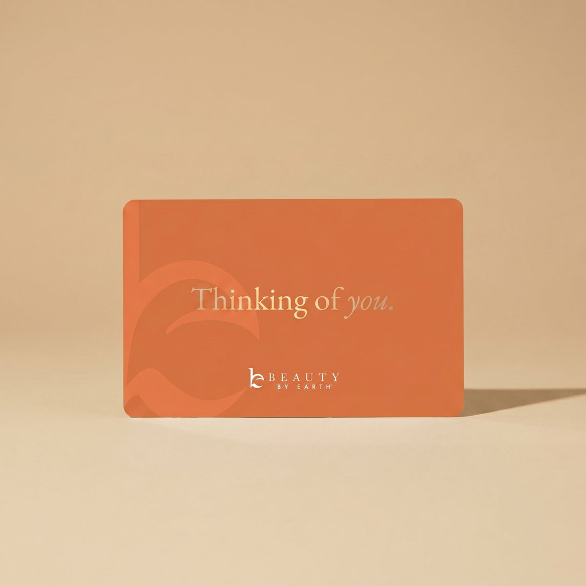 Orange card with 'Thinking of you' text and 'Beauty by Earth' logo on a beige background