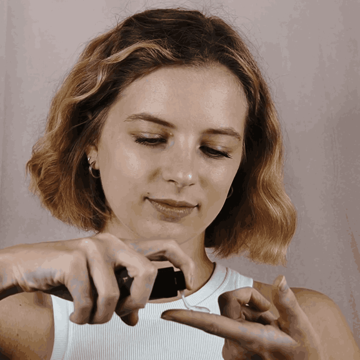 Woman holding a small object close to her face against a neutral background