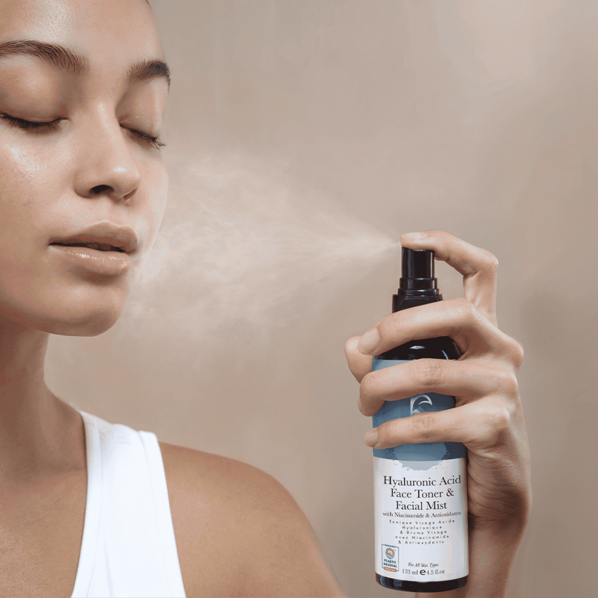 Person using a bottle of facial mist with a neutral background