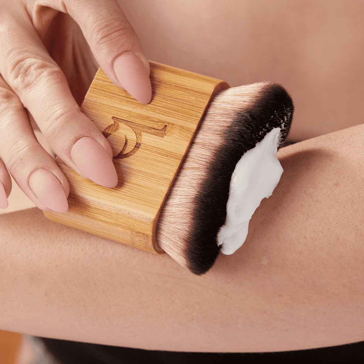 Person using a wooden brush with bristles on a person's arm, applying a white cream or lotion.