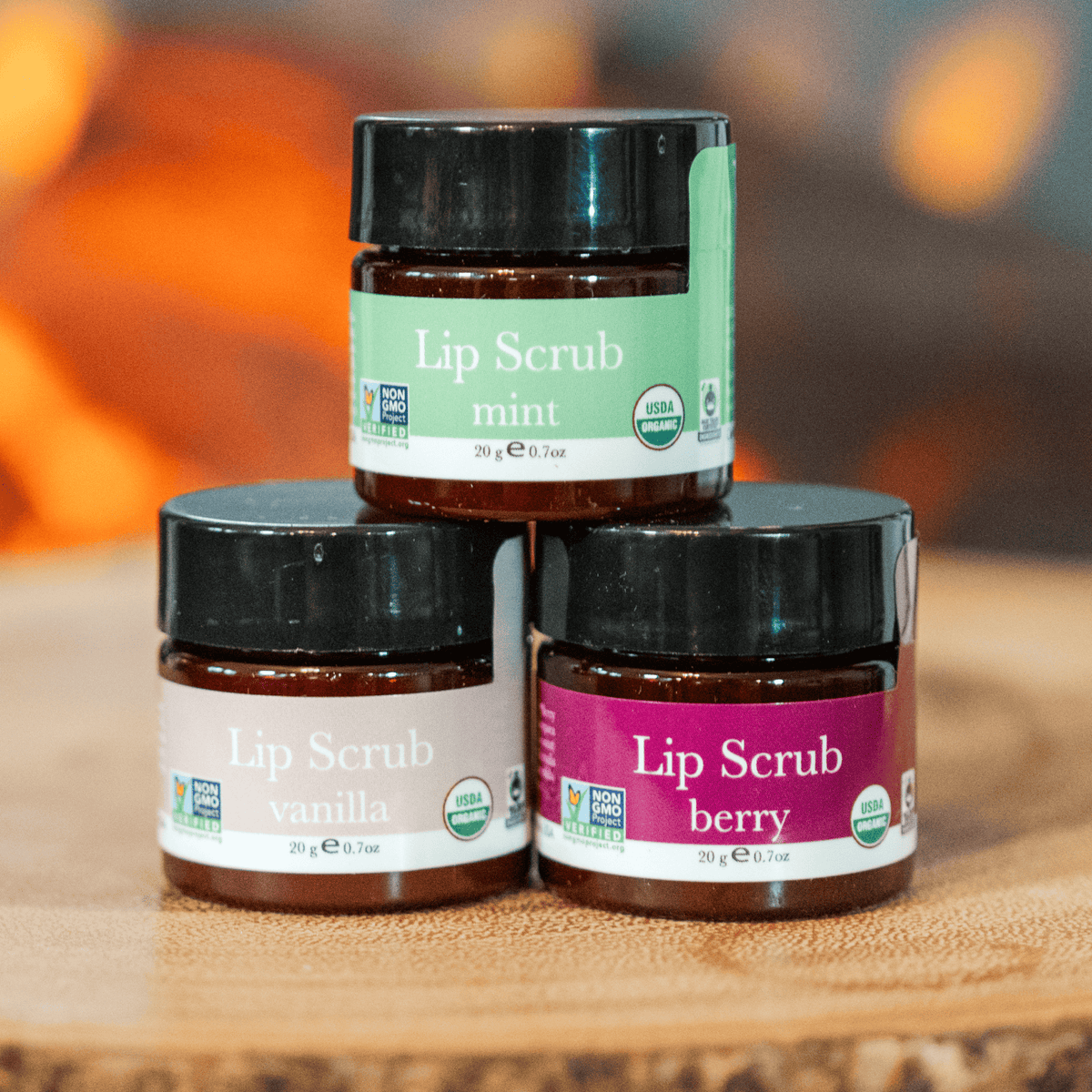 Three jars of lip scrub with different flavors on a wooden surface.