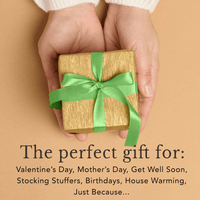 Hand holding a small gift box with a green ribbon on a beige background