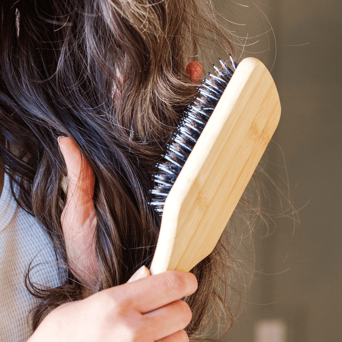 Person using a wooden hairbrush with bristles to detangle hair against a neutral background