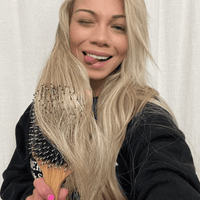 Woman with long blonde hair holding a hairbrush against a white background