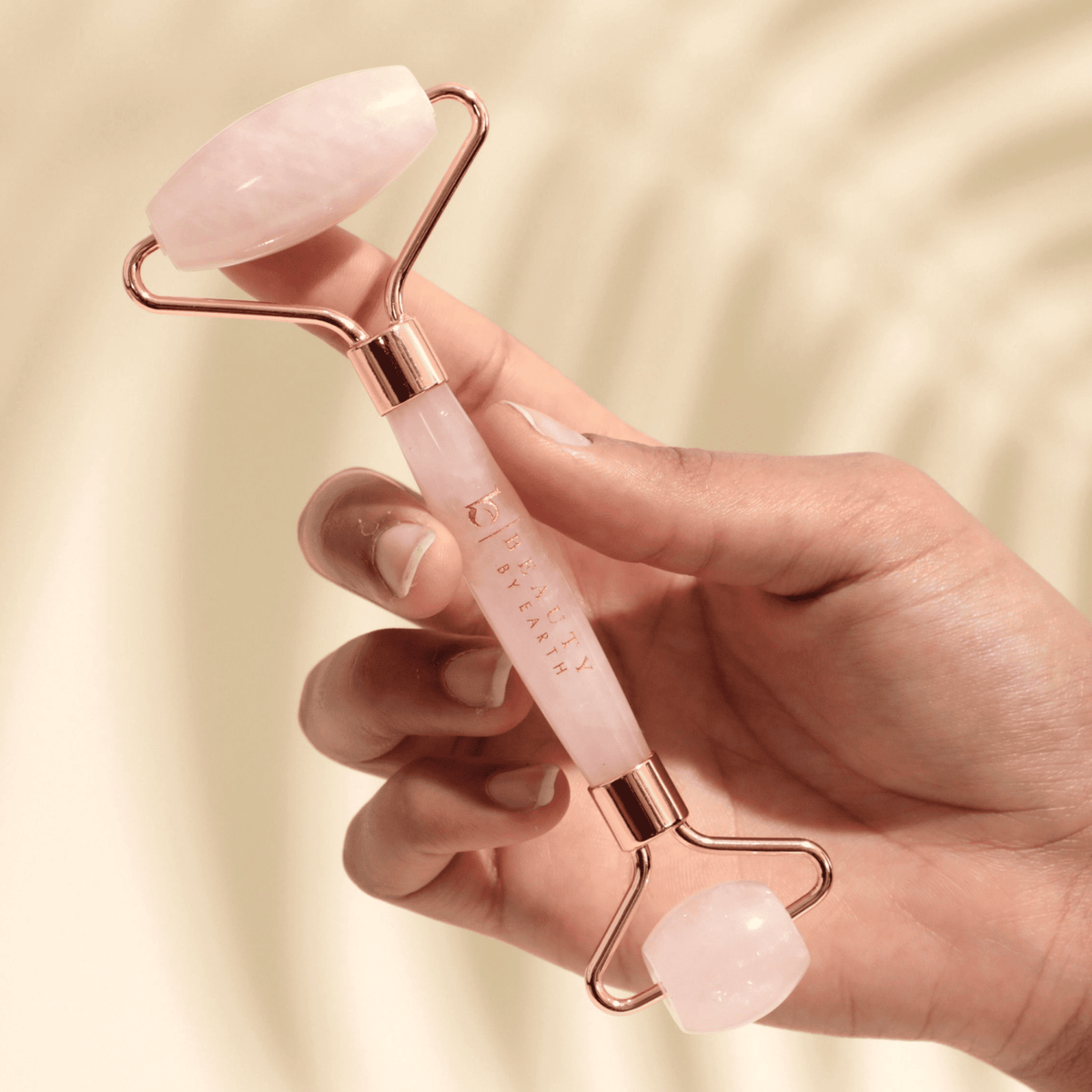 Hand holding a pink and rose gold skin care roller against a beige background