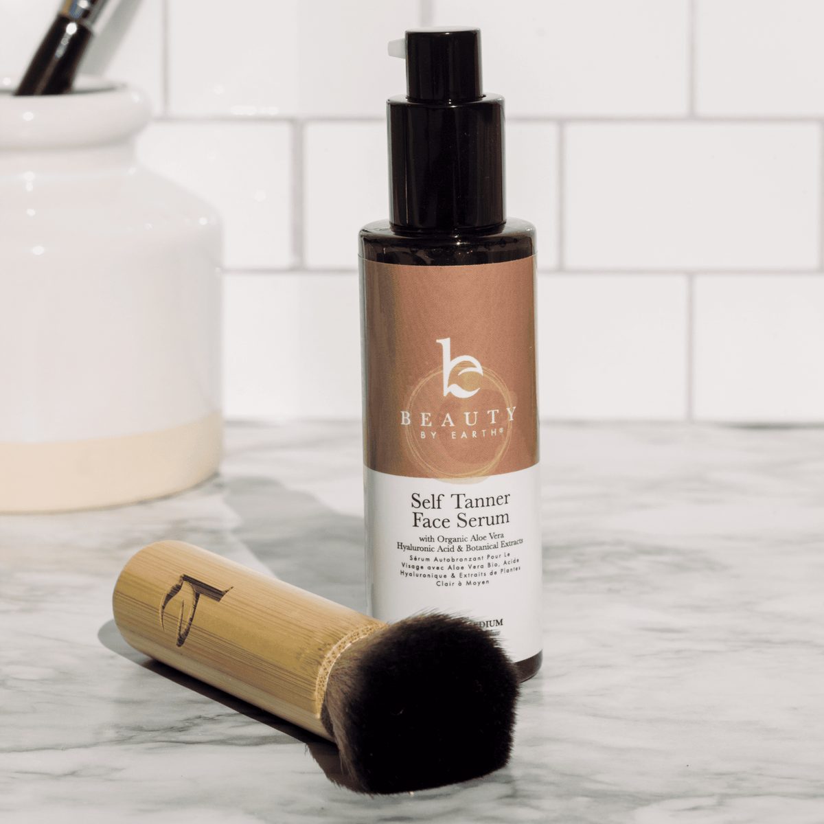 Beauty by Breimey self tanner face serum with a kabuki facial brush on a marble surface.