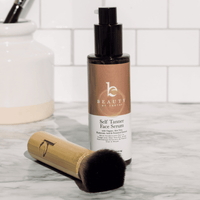 Beauty by Breimey self tanner face serum with a kabuki facial brush on a marble surface.
