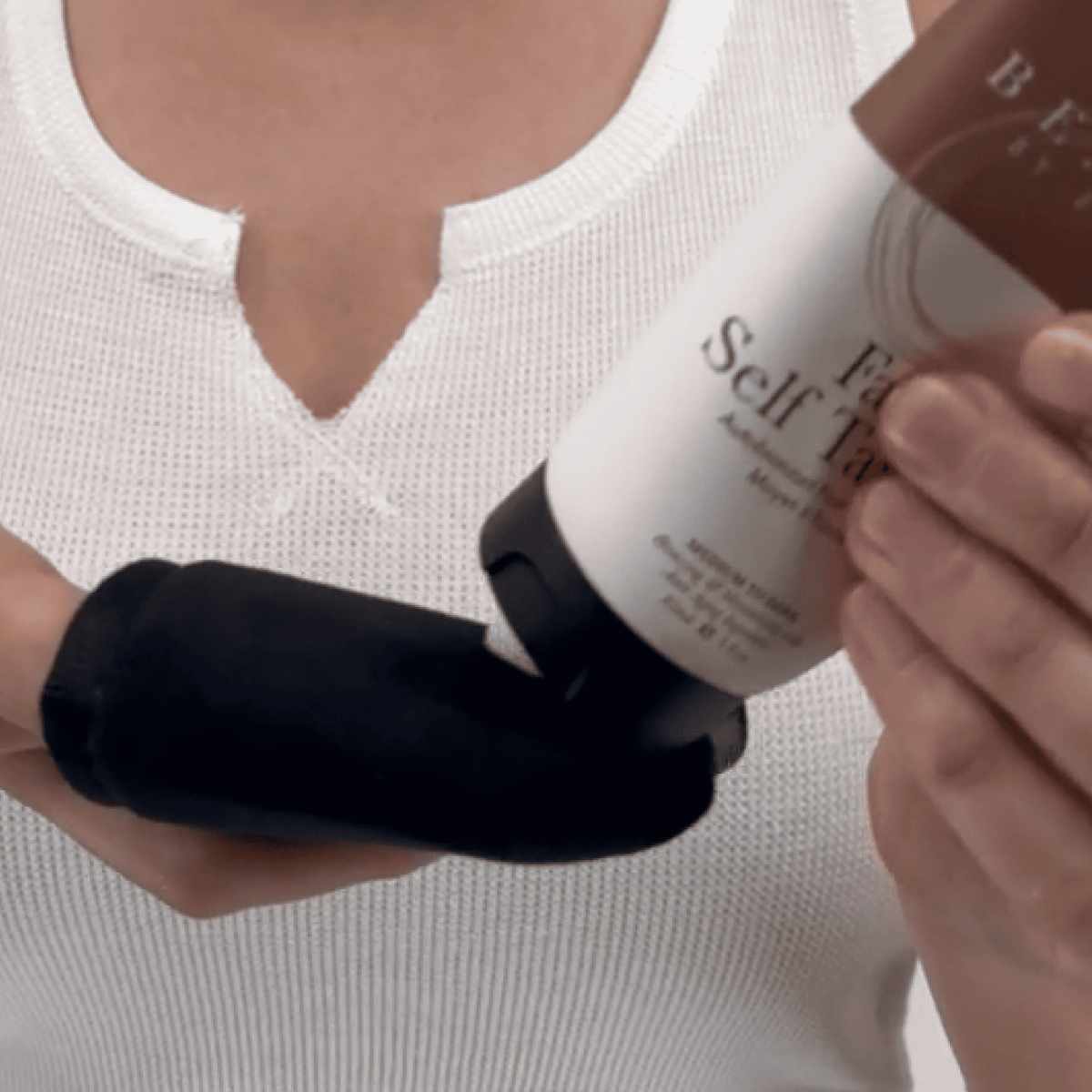 a model holding face self tanner lotion and face black mitt demo application.