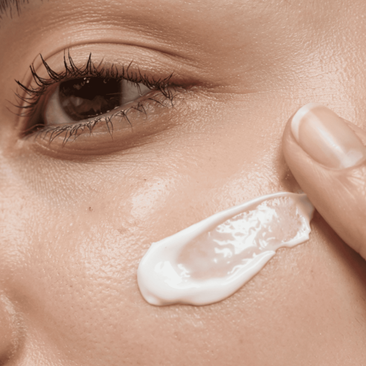 Close-up of a hand applying cream to the skin near an eye