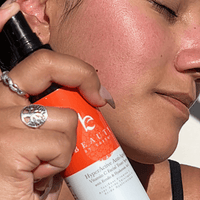 Person applying a skincare product to their face with a bottle labeled 'Vc Beauty'.
