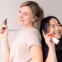 Two women holding skincare products against a plain background