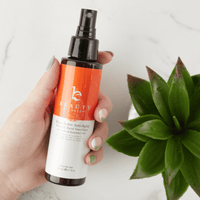 Hand holding a bottle of skincare product with a plant in the background