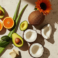 Fruits including coconuts, oranges, and avocados on a textured surface with a flower.